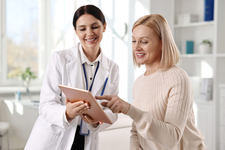 Profissional de saúde mostrando informações em um tablet para uma mulher durante consulta em consultório médico